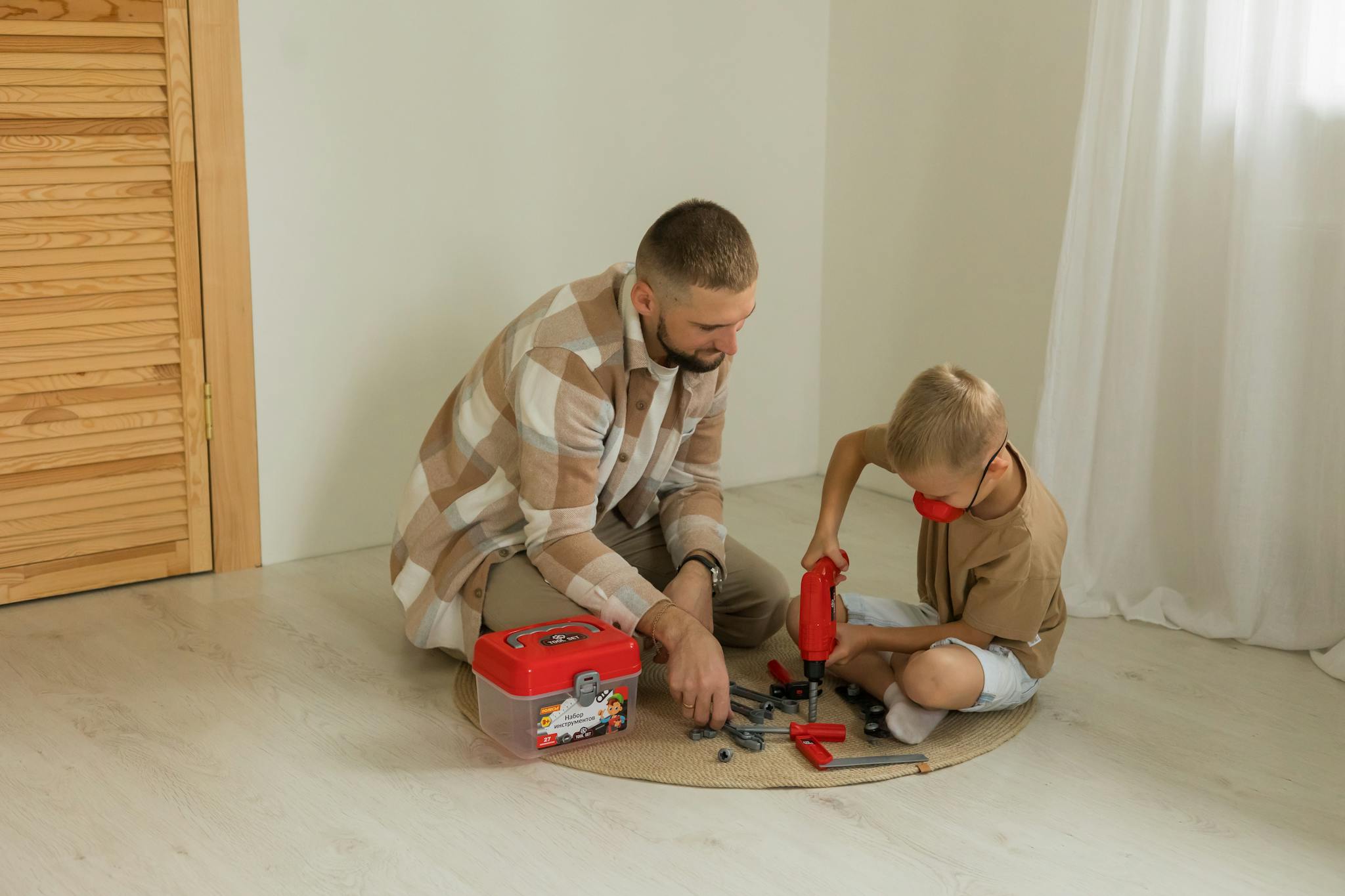 A father and son bonding over a building project with toy tools on a rug indoors.