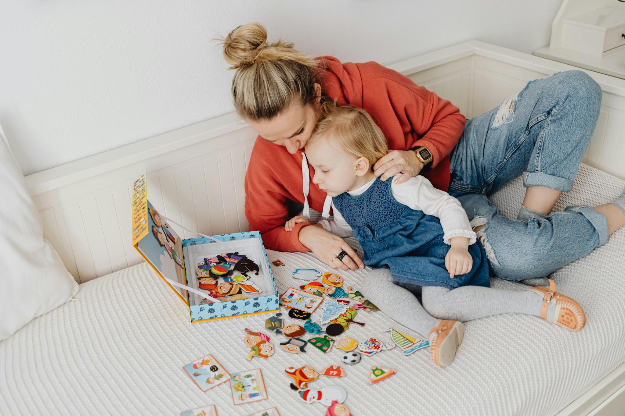 Mother and toddler enjoying playtime with colorful board game pieces on bed.
